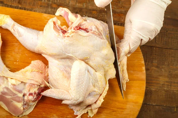 A female hand cuts off chicken pieces with a sharp knife.