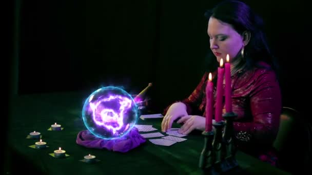 Der Wahrsager im Zaubersalon mischt und teilt Karten neben der Kugel aus, in der sich magisches Feuer auf schwarzem Hintergrund befindet.. — Stockvideo