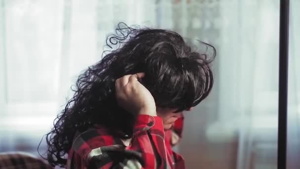 Uma mulher na frente de um espelho coloca uma peruca de palhaço com cachos pretos — Vídeo de Stock