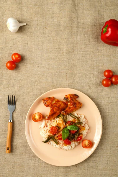 Bakade kycklingvingar i tomatsås med ris och grönsaker på en tallrik på en duk. — Stockfoto