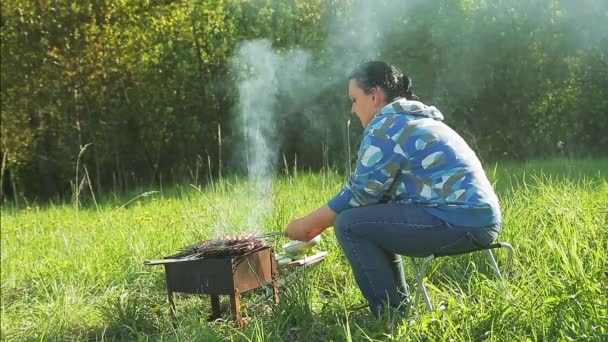 Egy nő a természetben húst és kolbászt süt a grillen.. — Stock videók