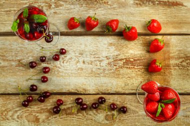 İçinde çilek, kiraz suyu ve taze böğürtlen bulunan iki kristal bardak ve içinde nane şekeri olan ahşap bir masa ve masa çerçevesinde böğürtlen..