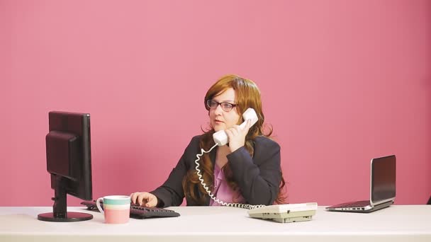 Νεαρή προϊσταμένη στο γραφείο μιλάει στο τηλέφωνο και πληκτρολογεί στον υπολογιστή. — Αρχείο Βίντεο
