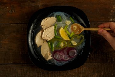 Siyah bir tabak Vietnamlı Pho çorbası. Tahta bir masada tavuklu kaşık..