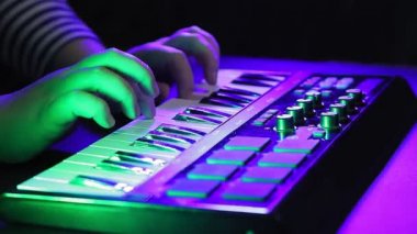 Kadın elleri bir MIDI klavyesinde çalıyor, dizüstü bilgisayar izlerken müzik kaydediyor