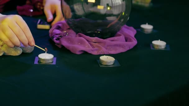 Un adivino en un salón mágico enciende velas sobre un fondo negro — Vídeo de stock