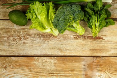 Yeşil sebzeler, brokoli, avokado, soğan, kaba tahtalardan bir masada ıspanak..