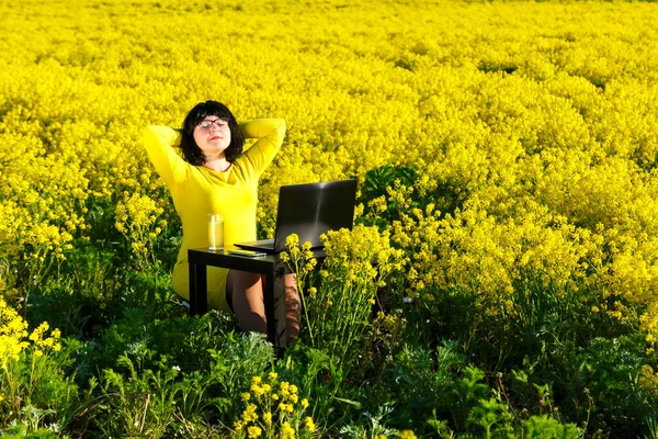 Ung kvinna frilansare vilar i ett fält bland gula blommor vid bordet. — Stockfoto