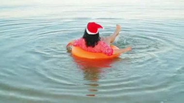 Yüzme çemberindeki esmer bir kadın ve Noel Baba şapkası Noel 'i ve yılbaşını denizde geçirir.