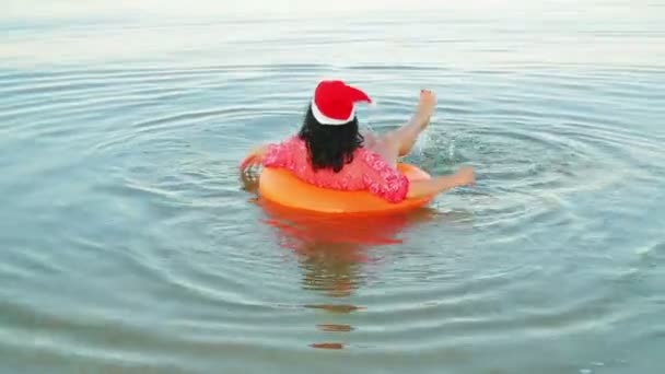 Brunetka w kręgu pływackim i kapelusz Świętego Mikołaja spędzają Boże Narodzenie i Nowy Rok na morzu — Wideo stockowe