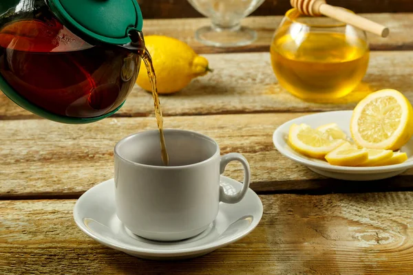 Frischer Tee aus der Teekanne wird in eine weiße Tasse gegossen. — Stockfoto