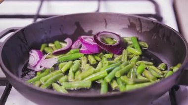 Bir kadın eli kızarmış yeşil fasulye tavasına kırmızı soğan ekler.