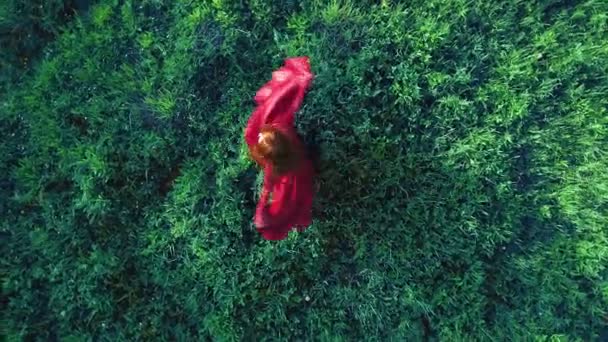 Den rödhåriga zigenaren i röd klänning snurrar på gräset på fältet. — Stockvideo