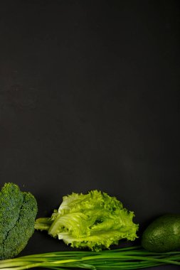 Siyah arka planda yeşil sebze, brokoli, avokado, soğan, ıspanak ve salata..