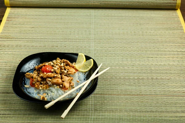 Plato con funchose y pollo con verduras en salsa tailandesa almohadilla junto a palillos en una estera de bambú . — Foto de Stock