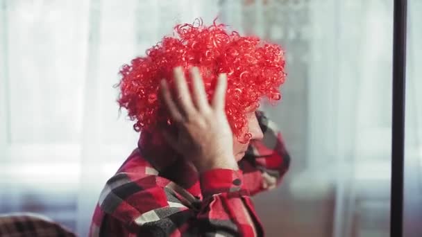 Un homme devant un miroir met une perruque de clown avec des boucles blanches. — Video