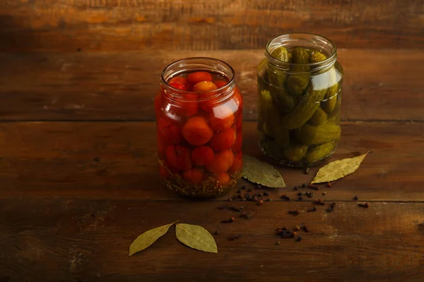 Frascos de pepinos en escabeche y tomates caseros y especias espolvoreadas sobre una mesa de madera . —  Fotos de Stock