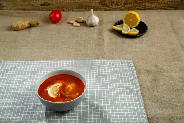 Sopa de Tom yum con pollo en un plato sobre un mantel en una servilleta de lino al lado de ajo y limón . — Foto de Stock