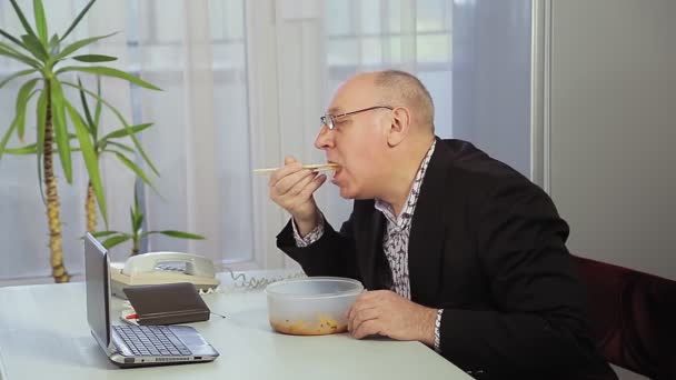 Um líder masculino na pausa para o almoço janta com a ajuda de pauzinhos chineses e fala ao telefone — Vídeo de Stock