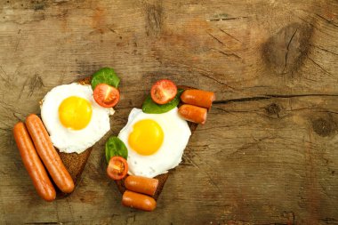 İki sandviç, sosisli sahanda yumurta ve ahşap bir masanın üzerinde otlu domates..
