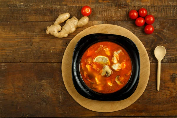 Soupe traditionnelle thaïlandaise Tom Yum au poulet dans une assiette noire sur un support en bois avec une cuillère. Espace de copie. — Photo