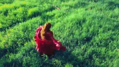 Kırmızı elbiseli kızıl saçlı çingene tarladaki çimlerin üzerinde dönüyor.