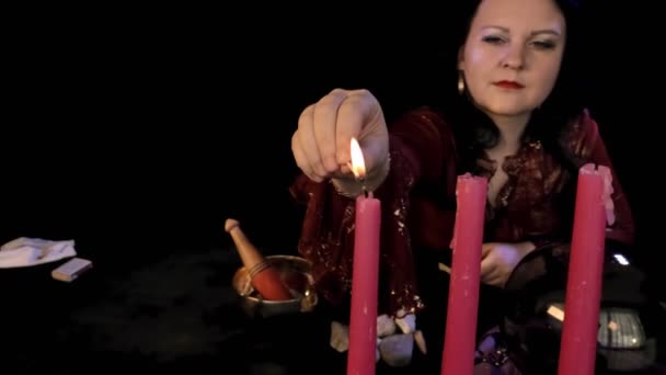 Um vidente em um salão mágico acende uma vela com um fósforo em um fundo preto — Vídeo de Stock