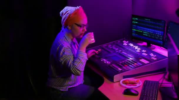 Een joodse vrouw in een hoofddoek, een lichtontwerper, programmeert het licht voor een show en drinkt koffie — Stockvideo