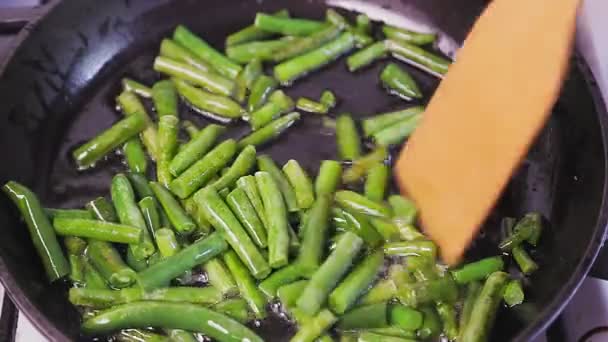 Τα πράσινα φασόλια τηγανίζονται σε ένα τηγάνι σε βραστό λάδι και αναμειγνύονται με μια ξύλινη σπάτουλα — Αρχείο Βίντεο