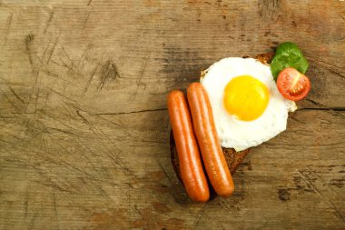 Sosisli sahanda yumurta ve ahşap bir masada bir parça ekmek üzerinde otlu domates..