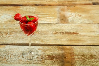 Çilek suyu ve taze böğürtlenli kristal bardak ve içinde nane şekeri olan ahşap masa..