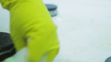 Lastik eldivendeki bir el gaz sobasının yüzeyindeki kiri süngerle ve köpüklü deterjanla temizler.