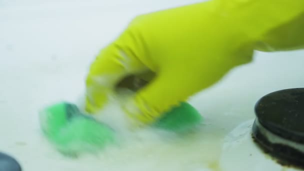 Рука в резиновой перчатке смывает грязь с поверхности газовой плиты губкой и моющим средством с пеной . — стоковое видео