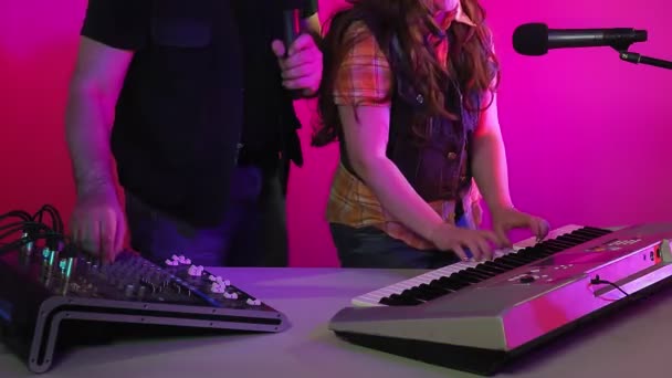 En man och en kvinna i en inspelningsstudio sjunger i en mikrofon. Hon spelar synthesizer. — Stockvideo