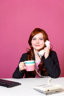 Ofiste genç bir kadın çay içiyor ve telefonda konuşuyor..