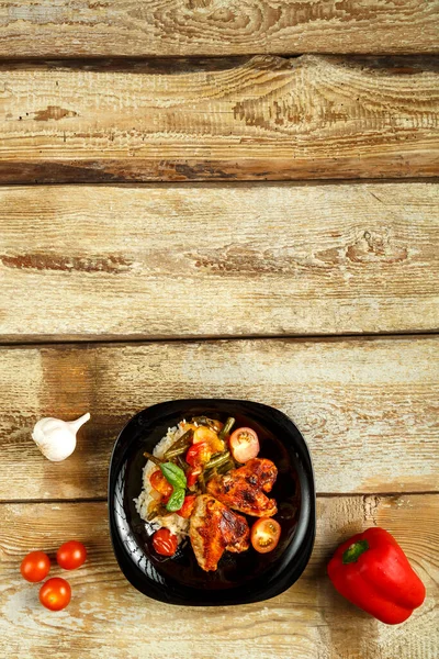 用番茄酱烤鸡翅，在靠近蔬菜的木制桌子上的黑色盘子里放上米饭和蔬菜. — 图库照片