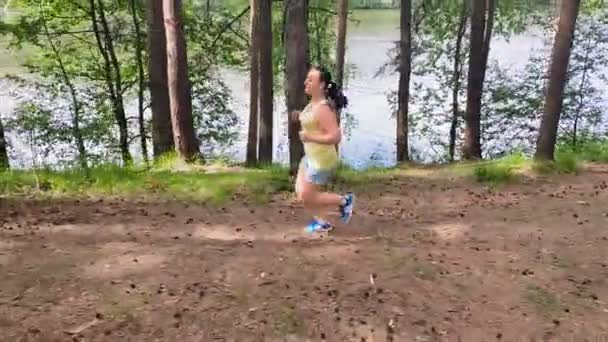 Een jonge vrouw in sportkleding jogt in een park langs de rivier.. — Stockvideo