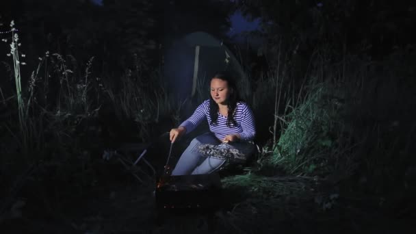 Een vrouw 's avonds in het donker bij een vuur in het bos friet vlees op de grill — Stockvideo