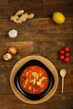 Geleneksel Thai Tom yer elması çorbası. Yanında bir kaşık ve sebzeyle birlikte ahşap bir stantta siyah bir tabakta tavuk var. Dikey fotoğraf