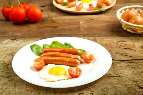 Breakfast a plate with fried egg with sausages and tomatoes on a wooden table. — Stock Photo, Image