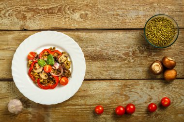 Ahşap bir masada, içinde mantar ve sebzeler bulunan kaynamış bir fasulye tabağı var..