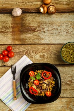 Ahşap bir masanın üzerinde, peçete ve çatal üzerinde sebze ve mantar bulunan siyah bir tabak masha var. Boşluğu kopyala.