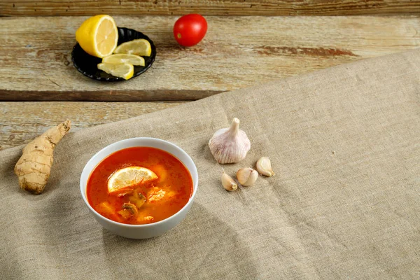 Sopa de Tom yum con pollo en un plato sobre un mantel en una servilleta de lino al lado de ajo y limón . —  Fotos de Stock