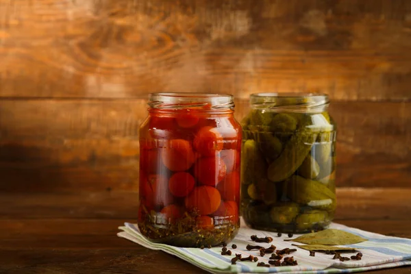 Burkar med inlagda hemmagjorda pickles och körsbärstomater och strödda kryddor på en linnehandduk på ett träbord. — Stockfoto