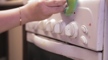 Deterjanlı kadın eli, paneli sobanın anahtarlarıyla yıkıyor.