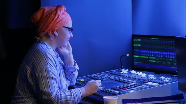 Una mujer judía con pañuelo y gafas, diseñadora de iluminación, programa la luz para el espectáculo — Vídeo de stock