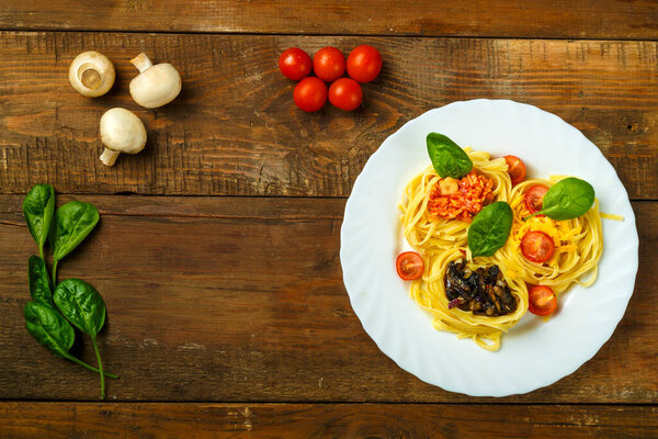 Plate of pasta nests stuffed with assorted pasta paste, cheese with cherry and fried mushrooms next to vegetables.