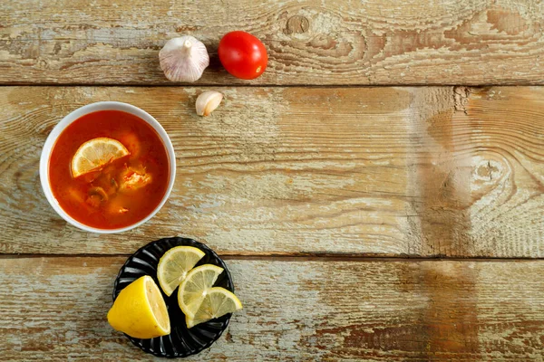 Un plat avec soupe thai tom yam sur une table en bois et ail et citron à proximité. — Photo