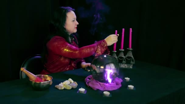 Un adivino en un salón mágico enciende velas en un candelero sobre un fondo negro — Vídeo de stock