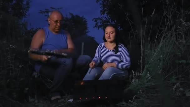 Одружена пара ввечері в темряві біля багаття біля намету в лісі гриль м'ясо на грилі . — стокове відео